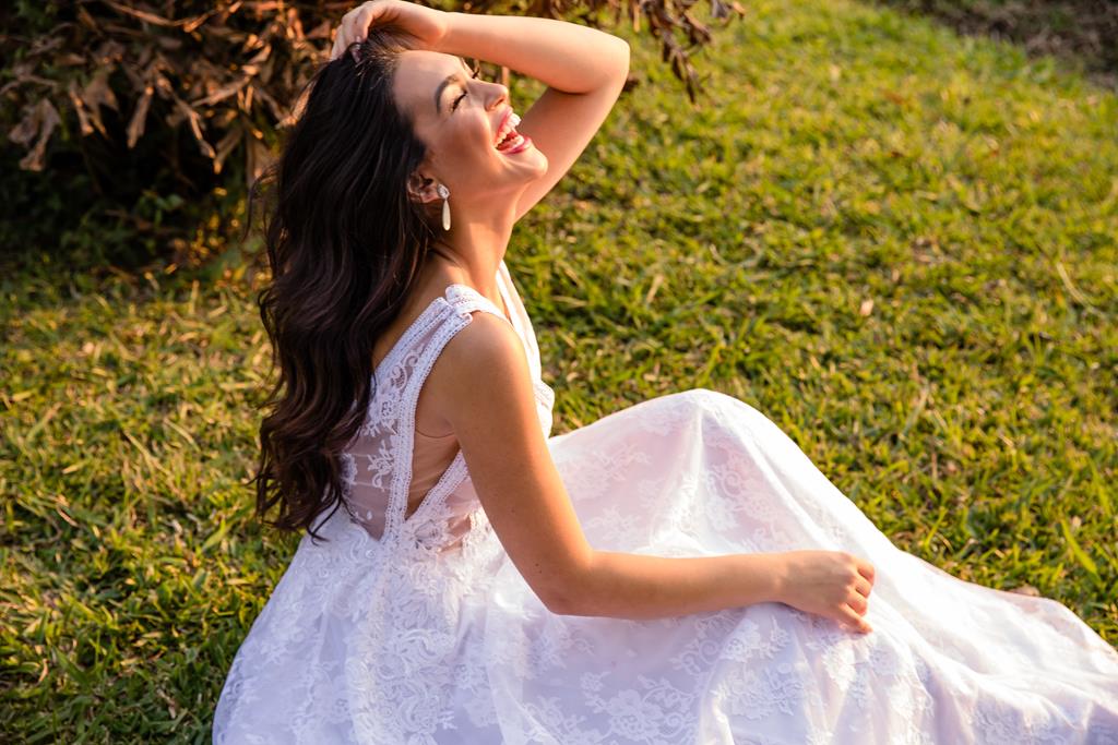 Foto de uma noiva sentada na grama em um jardim, sorrindo