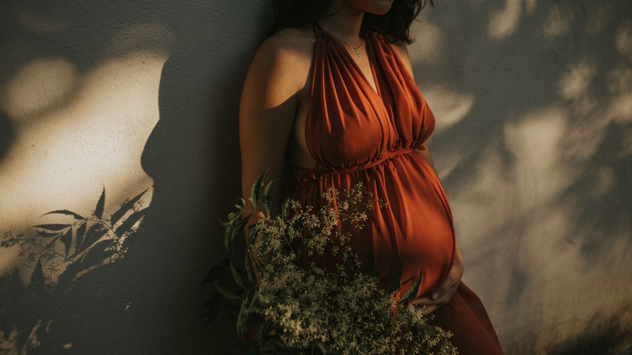 mulher grávida com vestido vermelho segurando um buquê de flores