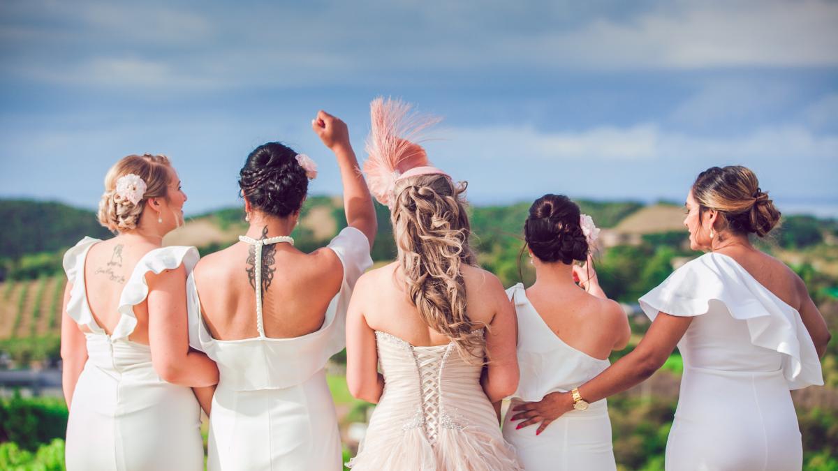Noiva e quatro madrinhas de costas usando vestidos brancos.