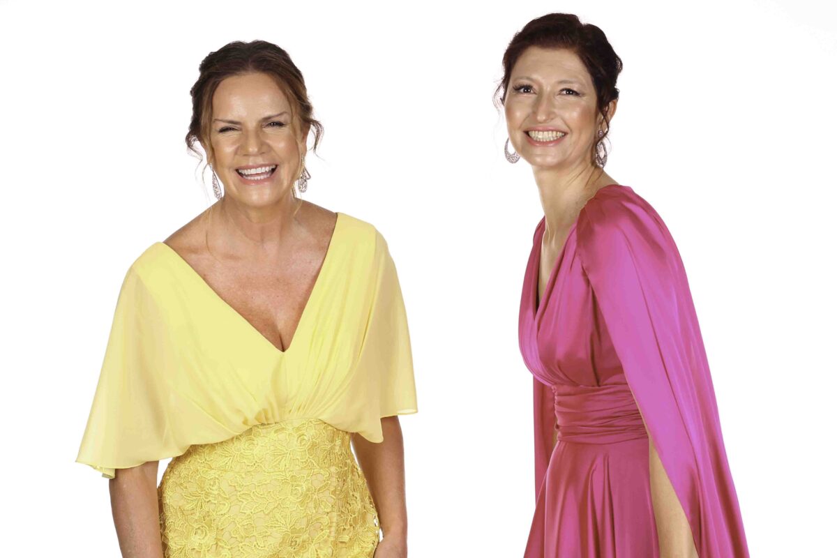 duas mulheres uma de vestido amarelo e outra de vestido rosa representando as mães dos noivos