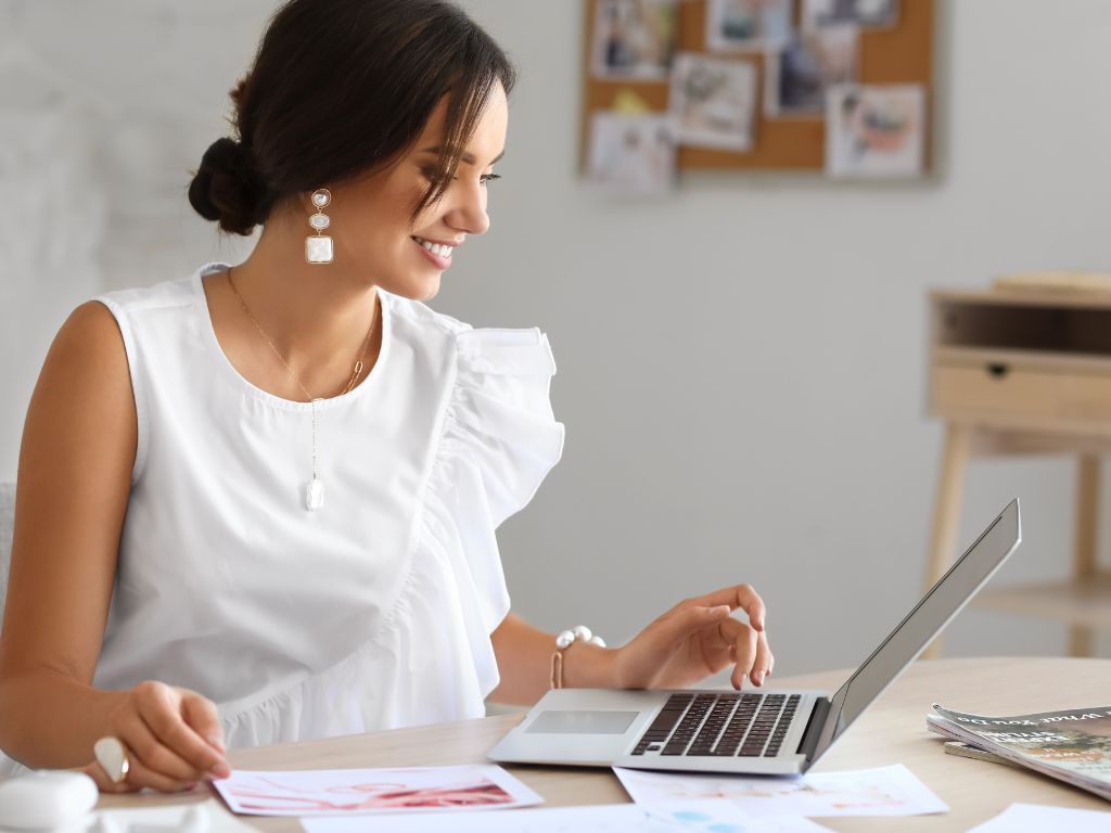 mulher com roupa branca sorrindo olhando para a tela de um notebook