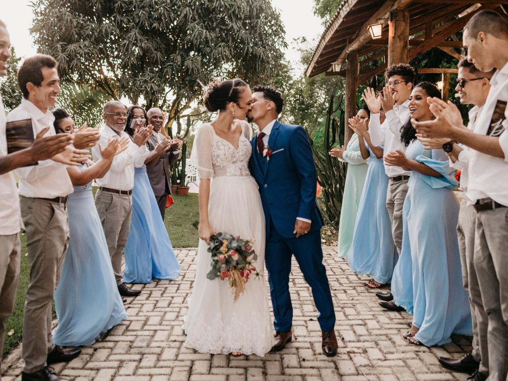 casal com trajes de casamento no centro se beijando e convidados ao redor