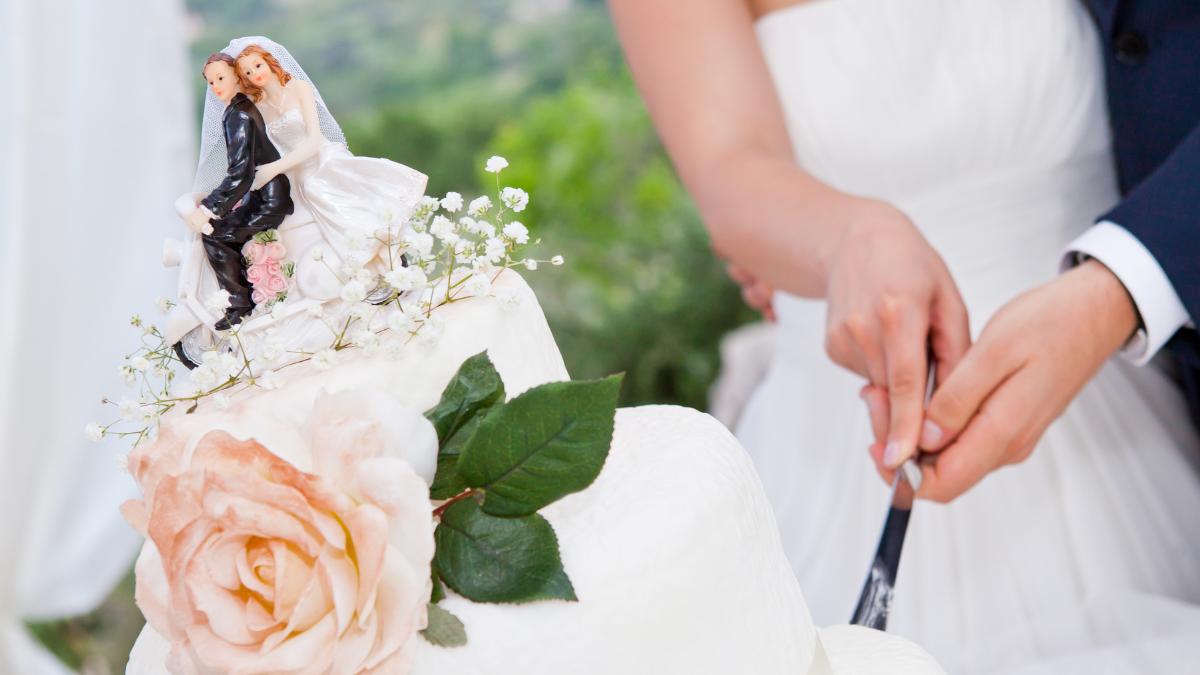 Casal cortando bolo de casamento decorado com flores e bonecos.