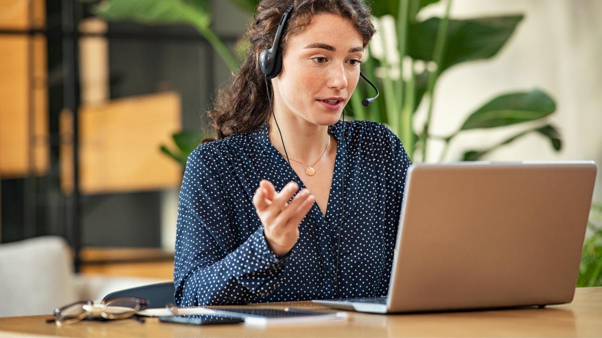 mulher com camisa azul de bolinhas olhando para um notebook e com fone