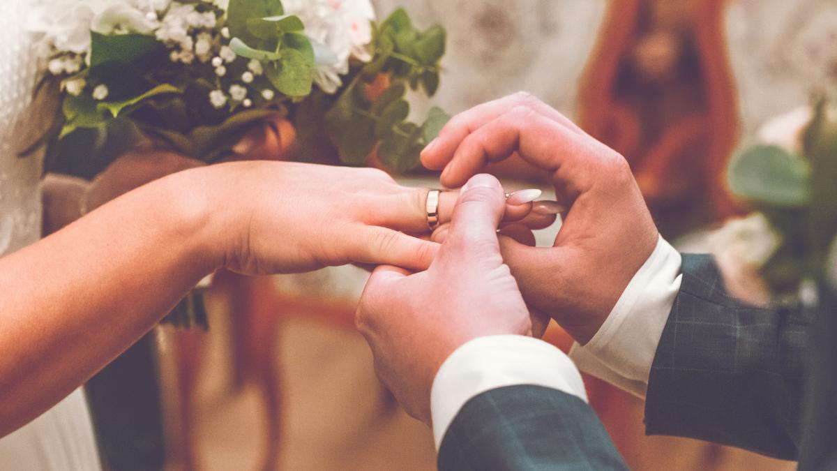 Casal de mãos dadas com aliança nos dedos.