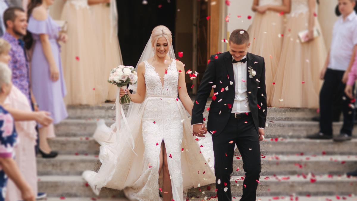 Casal saindo da igreja sendo recepcionado por pétalas de flores.