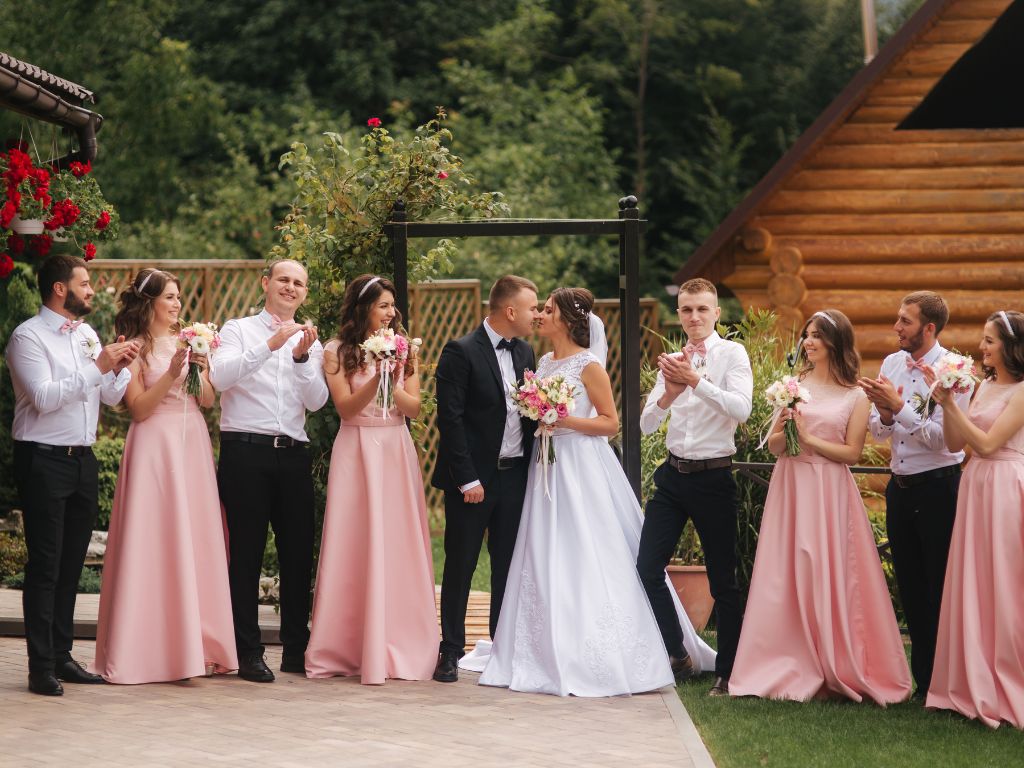 madrinhas de casamento vestidas de rosa, padrinhos e noivo ao centro se beijando