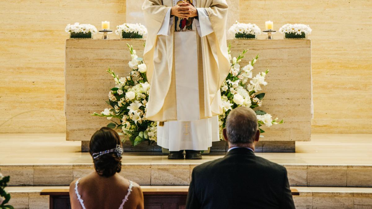 Noivos e padre em altar de igreja decorado.