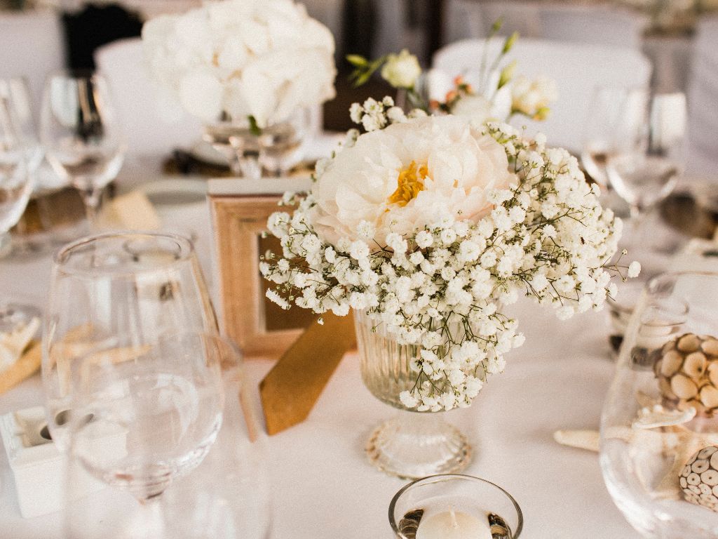 centro de mesa com flores brancas, taças e velas em uma mesa