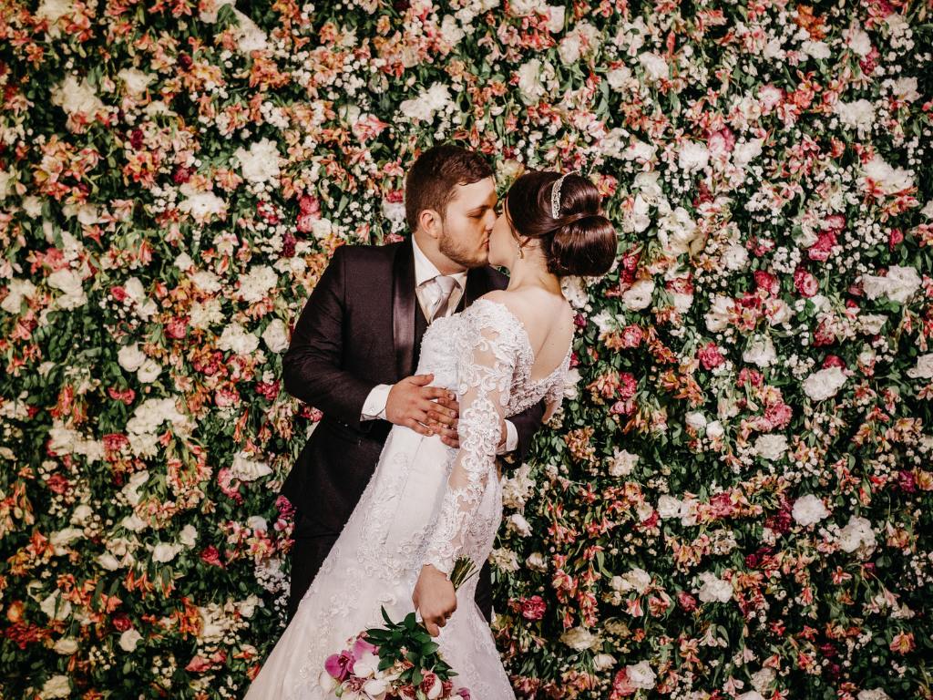 Casal se beijando em frente a painel de flores