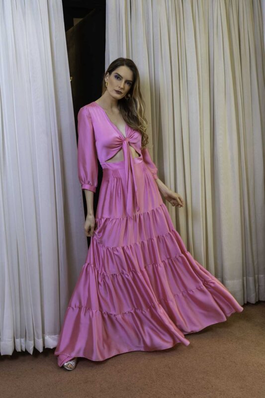 Fluidez do vestido de festa longo com saia de camadas de babados e manga longa com fechamento de laço na cor rosa, esse modelo é leve e elegante.