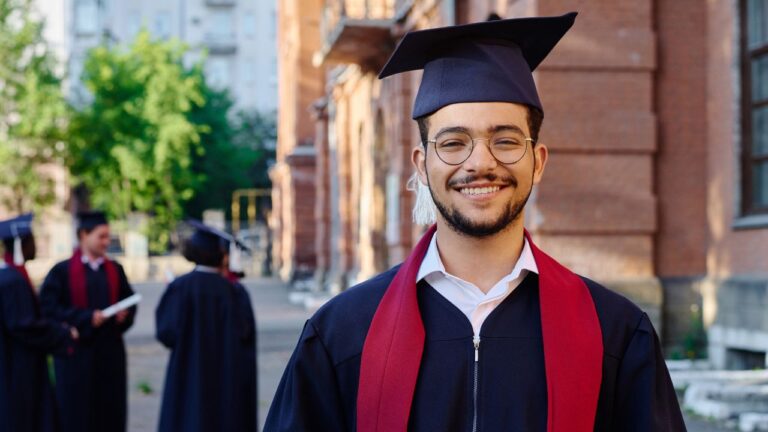 formando sorrindo vestido com beca e faixa vermelha