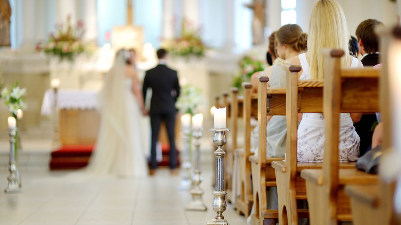 convidados em primeiro plano e noivos se casando na igreja católica no fundo