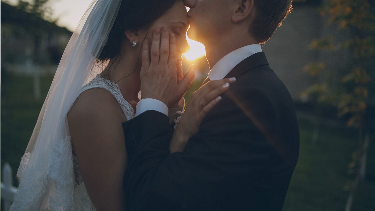 foto de casamento no estilo fine art com noivo beijando testa de noiva em um ambiente que parece um campo com a luz do sol bem evidente