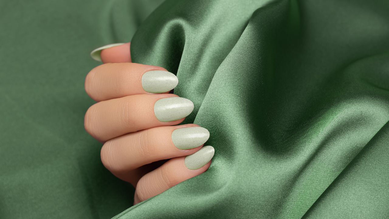 mão com unha verde clara segurando tecido verde